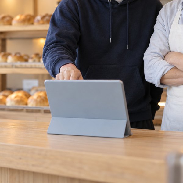 開店前のパン屋のカウンターで、店主とエンジニアがタブレットをのぞき込む