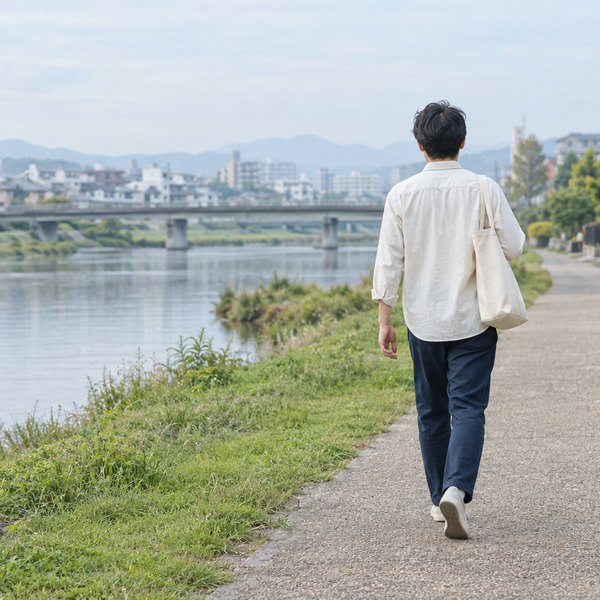 平日の朝、川沿いの遊歩道をトートバッグを提げて歩くエンジニアの後ろ姿